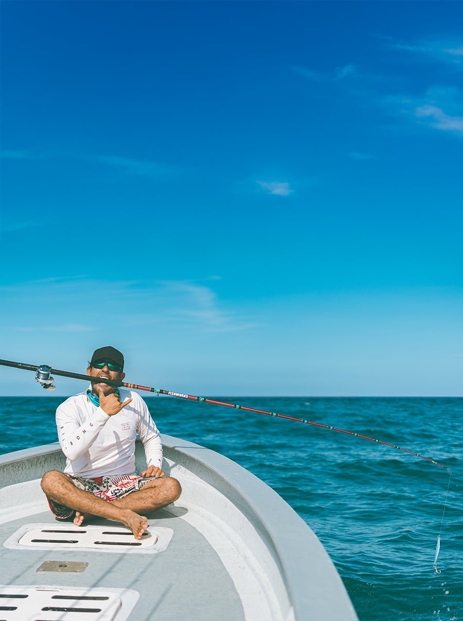 Man posing with his fishing rod on his teeth on a boat with clear blue sky and ocean