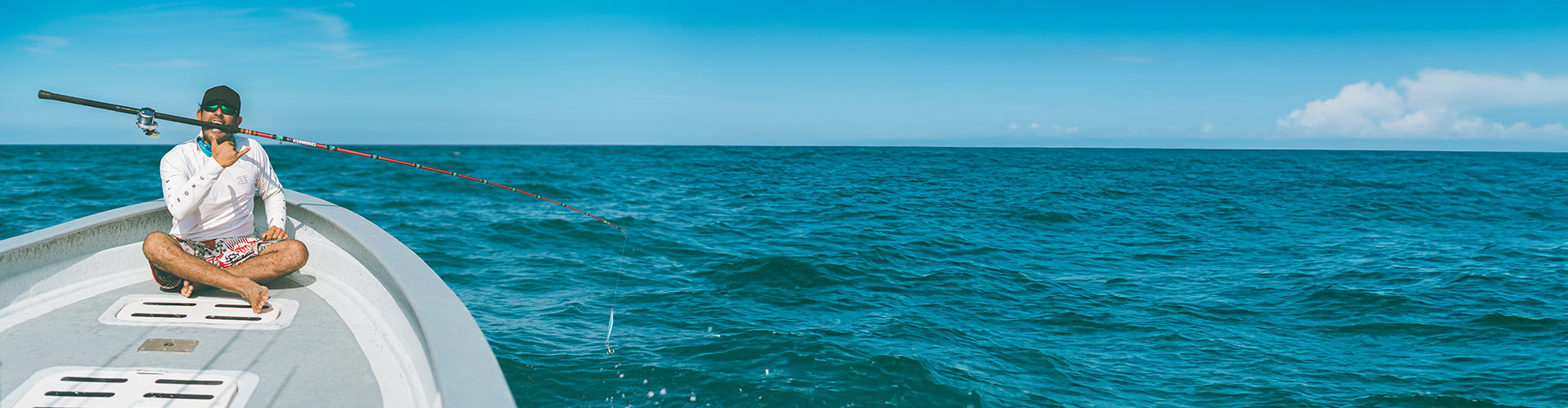 Person sitting on a boat biting on his fishing rod in the middle of the ocean with a clear blue sky 