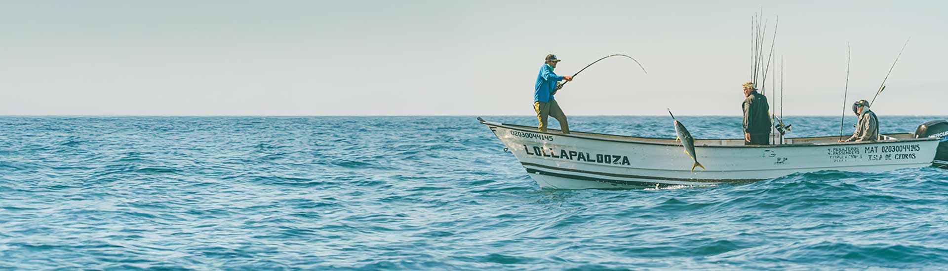 Two people fishing from a small boat on a calm ocean with clear skies.