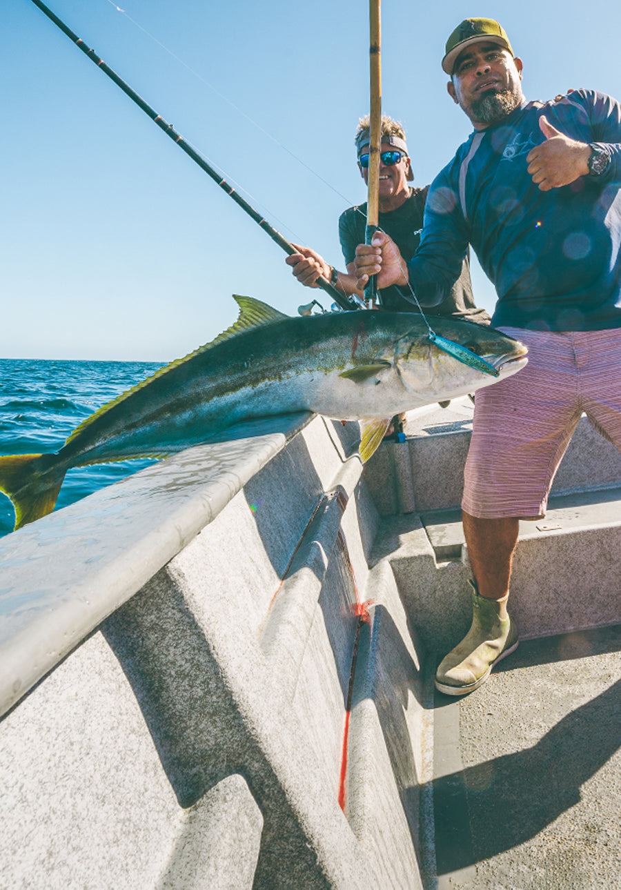 Two people on a boat with a large fish caught, holding it with a fishing rod.