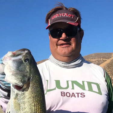 Man holding a fish with a lake in the background