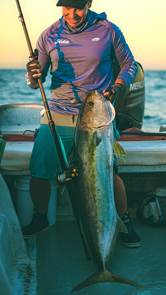 Man holding a large fish on a boat with a sunset background