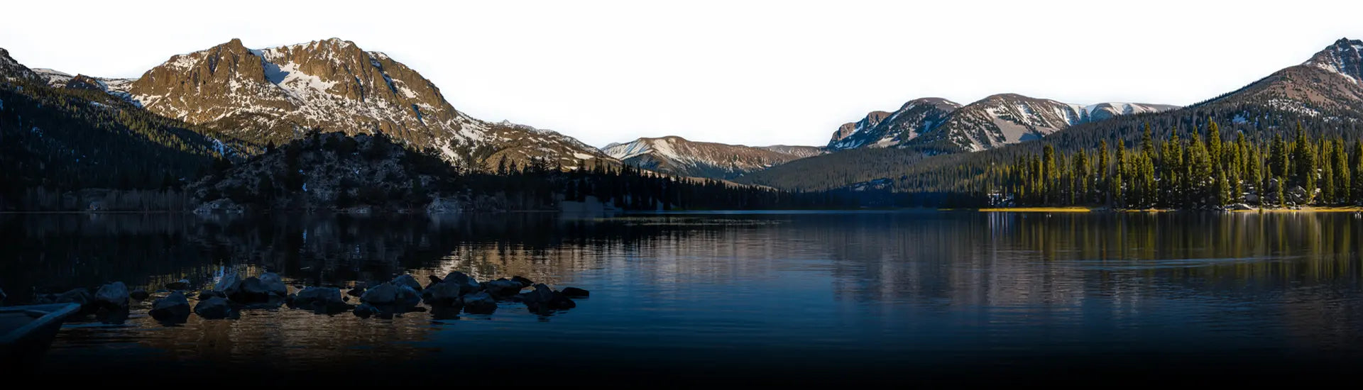 Panoramic view of a mountain lake with reflections and snow-capped peaks.