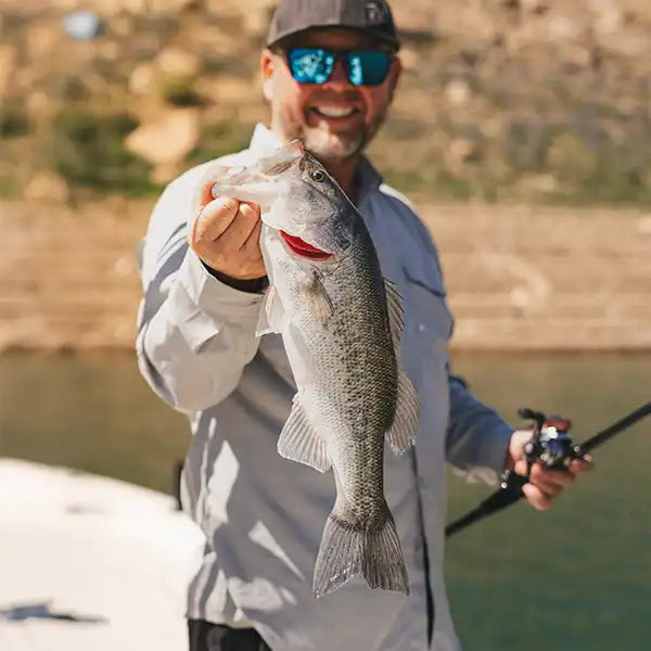 Chad holding a largemouth bass caught while fishing by a lake.