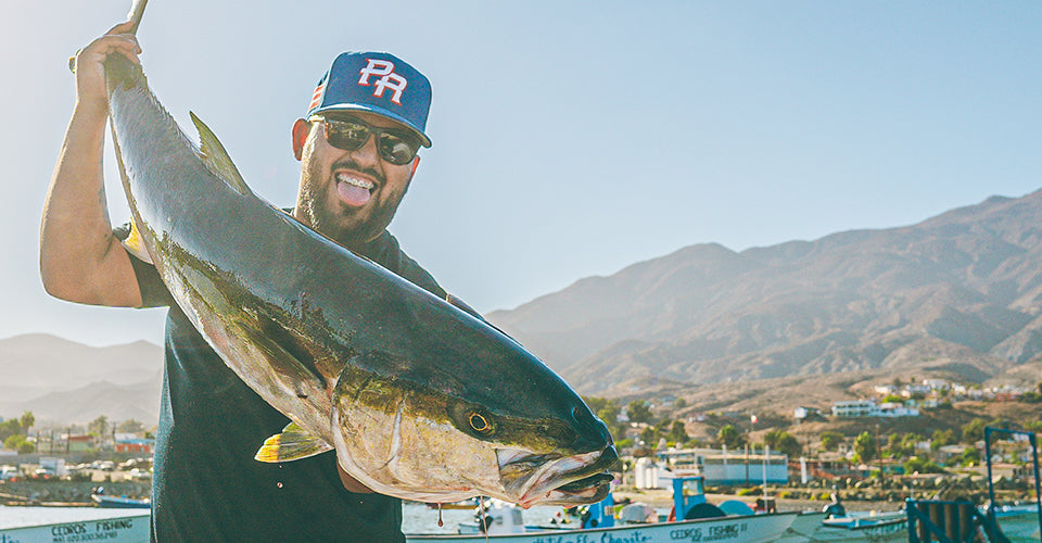 Man holding a large yellowtail with in a scenic outdoor setting